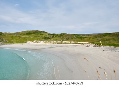 A view overlooking a sunny Mull beach and bay with waves, cows roaming and people walking along the sand. Beautiful scenery on the Isle of Mull, Scotland. Turquoise waters lap at the shore.