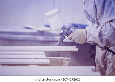 View Of The Paint Shop Of Carpentry. Man Painting Furniture Details. Toned Image. Using Spray Gun Close Up View