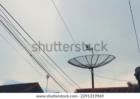 View of parabolic antenna and telephone wires with sky background