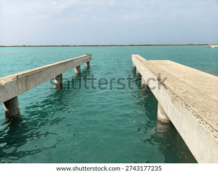 View of a parallel concrete pier structure extending into calm blue sea water under a clear sky