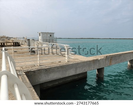 View of a parallel concrete pier structure extending into calm blue sea water under a clear sky