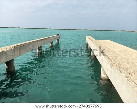 View of a parallel concrete pier structure extending into calm blue sea water under a clear sky