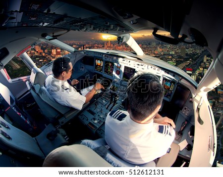 The view from the passenger aircraft cockpit. Pilots at work. The airplane climbs over the cityscape and skyscrapers at sunset.
