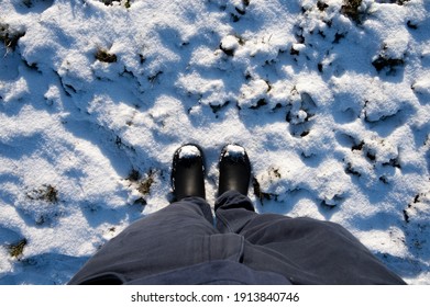 View Of Person Looking Down At Legs And Shoes Standing On Snow Covered Ground On Winter Day