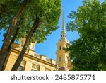 view of the Peter and Paul Cathedral and bell tower through trees of the park, in the Peter and Paul Fortress, at daytime, St Petersburg, Russia 