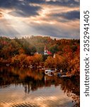 View of the picturesque village of Chelsea and its church during autumn, fall foliage with sunbeams piercing through clouds, Quebec, Canada. Photo taken in October 2022.