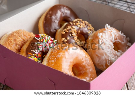 A view of a pink box filled with a half dozen favorite donut varieties.