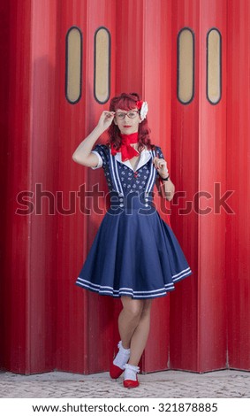 View of pinup young woman in vintage style clothing over a red metal door.