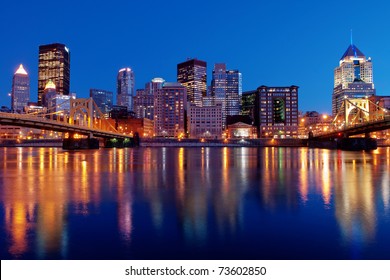 A View Of The Pittsburgh, Pennsylvania Cityscape At Night Overlooking The Allegheny River With Views Of The Roberto Clemente Bridge And Andy Warhol Bridge.