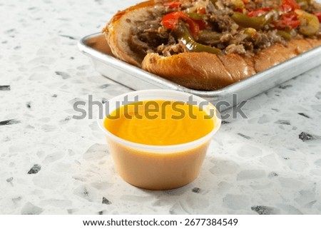 A view of a plastic condiment cup of cheese sauce for a Philly cheesesteak sandwich.