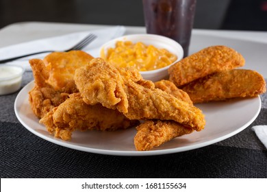 A View Of A Plate Of Breaded Chicken Tenders, With Potato Wedges And Macaroni And Cheese Sides.