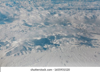 View From The Porthole Of An Airplane On The Mountains. 10.000 Meters Above Ground Level. White Snow Covered Mountain During Daytime.