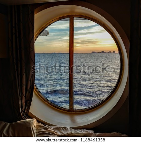 A view from the porthole window of a cruise ship, showing the city buildings in the sunset. The photo was taken inside a cabin on a Caribbean cruise.