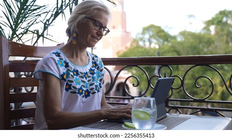 View of pretty happy mature woman digital nomad using a laptop tablet computer on a balcony in Europe with trees and church blurred in background. - Powered by Shutterstock