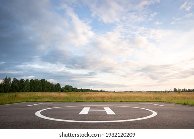 View of the private helipad on a warm summer evening. An asphalt helipad against the backdrop of a green field and a cloudy evening sky.
