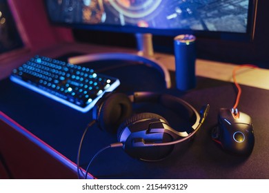 View of pro gaming desk setup with headset, keyboard, monitor and computer mouse illuminated by neon lights. Cyber sport equipment laying on desktop, ready for online video shooter games and streaming