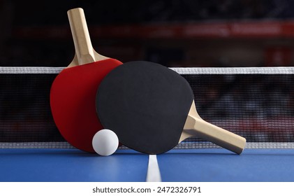 View of professional ping pong set with paddles resting on the net on green game table with white ball. Front view.