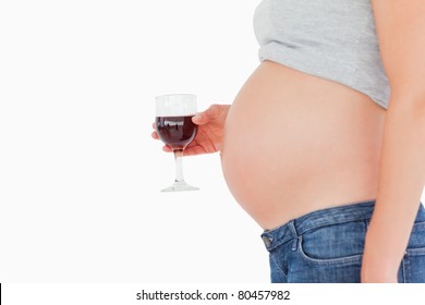 View profile of a pregnant woman holding a glass of red wine while standing against a white background