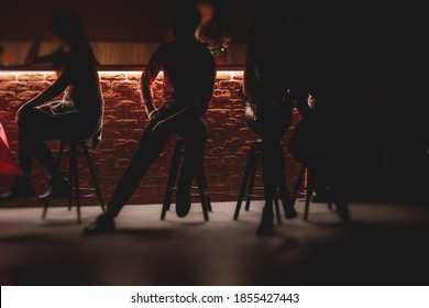 View of pub interior with people silhouettes drinking alcohol beverages and chatting at the bar counter, backlit illumination - Powered by Shutterstock