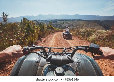 View from a quad bike in nature. Woman in front driving off road on an all terrain vehicle. POV image of a quad biker following another biker on a trail