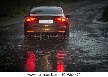View from a rain-drenched windshield on shower drenched back lights of a car in front. Heavy rain