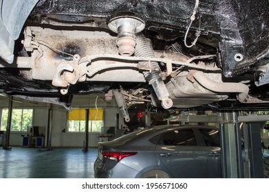 View Of The Rear Suspension Of The Car With The Rear Beam Removed. The Car Is Hanging On A Lift In An Auto Repair Shop.