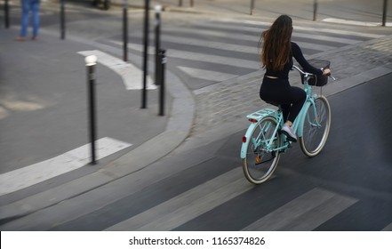 View From The Rear Of  Woman Cycling To Work In A City. Concept Of Eco-friendly Transport. Empty Basket. Girl With Long Brunette Hair Wear Black Dress