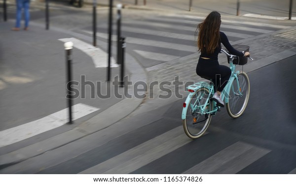 View from the rear of  woman cycling to\
work in a city. concept of eco-friendly transport. empty basket.\
girl with long brunette hair wear black\
dress