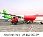 A view of a red and white aircraft fuel tanker truck next to a commercial aircraft being refueled with aviation fuel before takeoff.