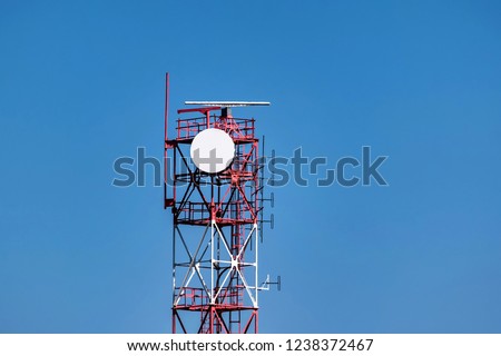 View of red and white communication tower against blue sky