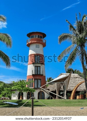 View of red and white lighthouse tower under blue sky among tropical palm trees. Sightseeing while wandering around beautiful Playa Venao in Panama. Incredible paradise location for holiday retreat.