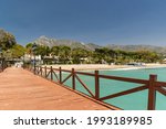 View of red wood bridge "Embarcadero" in Marbella. View of Luxury area Puente Romano, expensive urbanisations. Mountain "La Concha". Spectacular travel destination. Emerald water, no people