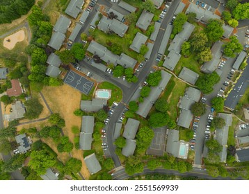 A view of a residential neighborhood with a pool and a basketball court. The houses are all lined up and there are many cars parked on the street - Powered by Shutterstock