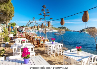 Blick auf Restaurant oder Café und Bougainvillea Blumen am Strand in Gumusluk, Bodrum Stadt der Türkei. Die Stühle, Tische und Blumen im Stil der Ägäis in Bodrum in der Nähe des schönen Ägäischen Meeres.