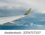 View of right wing from window of airplane flying up in the sky, through clouds in atmosphere. Plane in flight. Up in the air. Aviation business, airline miles, travel background and copy space.