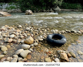 View Of A River With Stones And Old Inner Tube And Greens In The Background