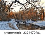 View of the river and yellow trees in a snow-covered park in late autumn