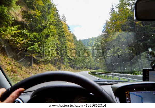 View of the road with a beautiful mountain\
landscape from the car window in a nice summer or autumn day.\
Woman\'s hand on the steering wheel. Female driver seeing beautiful\
landscape during travel