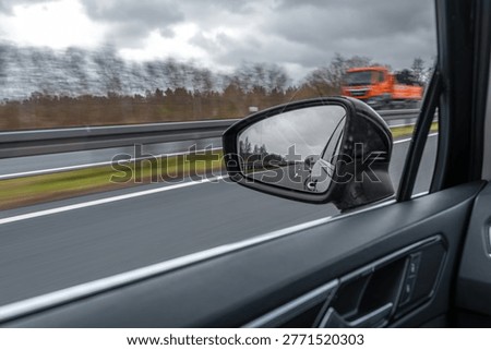 View of the road through a car side mirror. The vehicle moves on a highway in cloudy weather.