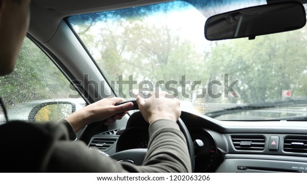 view of the road from the windshield\
of the car in the rain. Drops of water fall on the glass, making it\
difficult to view. the man holds the steering\
wheel.