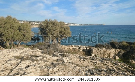 view of the rocky shore and town from nordsee in malta, sea on left side, buildings at right side, sky is blue with few clouds, camera angle looks over rocks to city, daylight, photo taken by phone