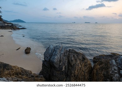 A view from a rocky shoreline looking out towards the calm ocean with distant islands in the background at sunset. - Powered by Shutterstock