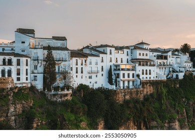 View of Ronda, Spain, with whitewashed buildings on a cliff. Traditional Spanish architecture with arched windows and terracotta roofs. Sunlit gorge below. - Powered by Shutterstock