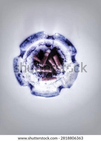 ​Top view of a round blue-patterned ceramic ashtray filled with burnt cigarette butts and ash isolated on a clean white background