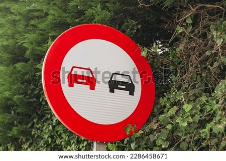 View of a round road sign with two cars drawn on it. Road sign on the background of green leaves