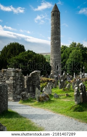 A view of the round tower in the graveyard in the Glendalough monastery in Co Wicklow Ireland set in a valley on a sunny day showing perfectly green natural countryside. Irish tourist attraction