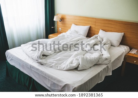 View of a rumpled bed with white pillows and a duvet.
