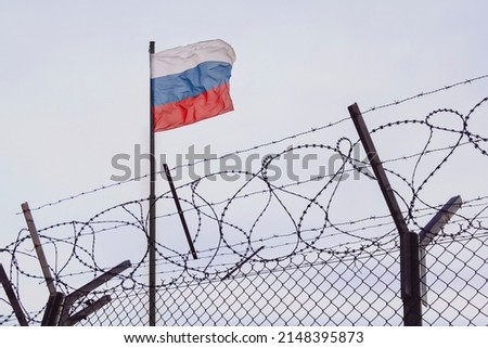 View of russian flag behind barbed wire against cloudy sky. Concept anti-Russian sanctions. A border post on the border of Russia. cancel culture Russia in the world