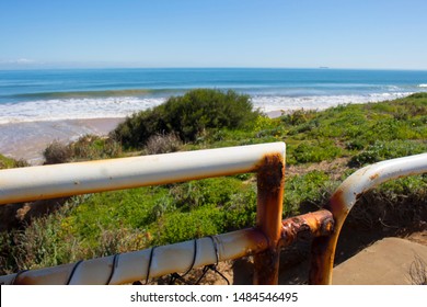 View Of The Rusted White Painted Metal Pipe Fence Near The Storm Water Drain At Ocean Beach, Bunbury, Western Australia In Late Winter.