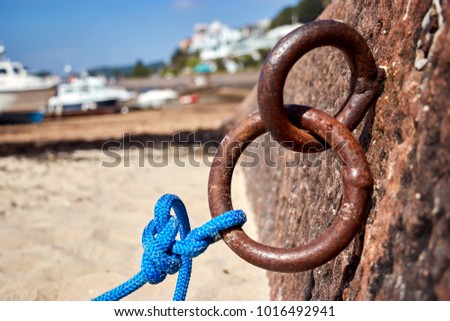 View of rusty rings in harbour wall with rope with blue sky and out of focus boats the background.
